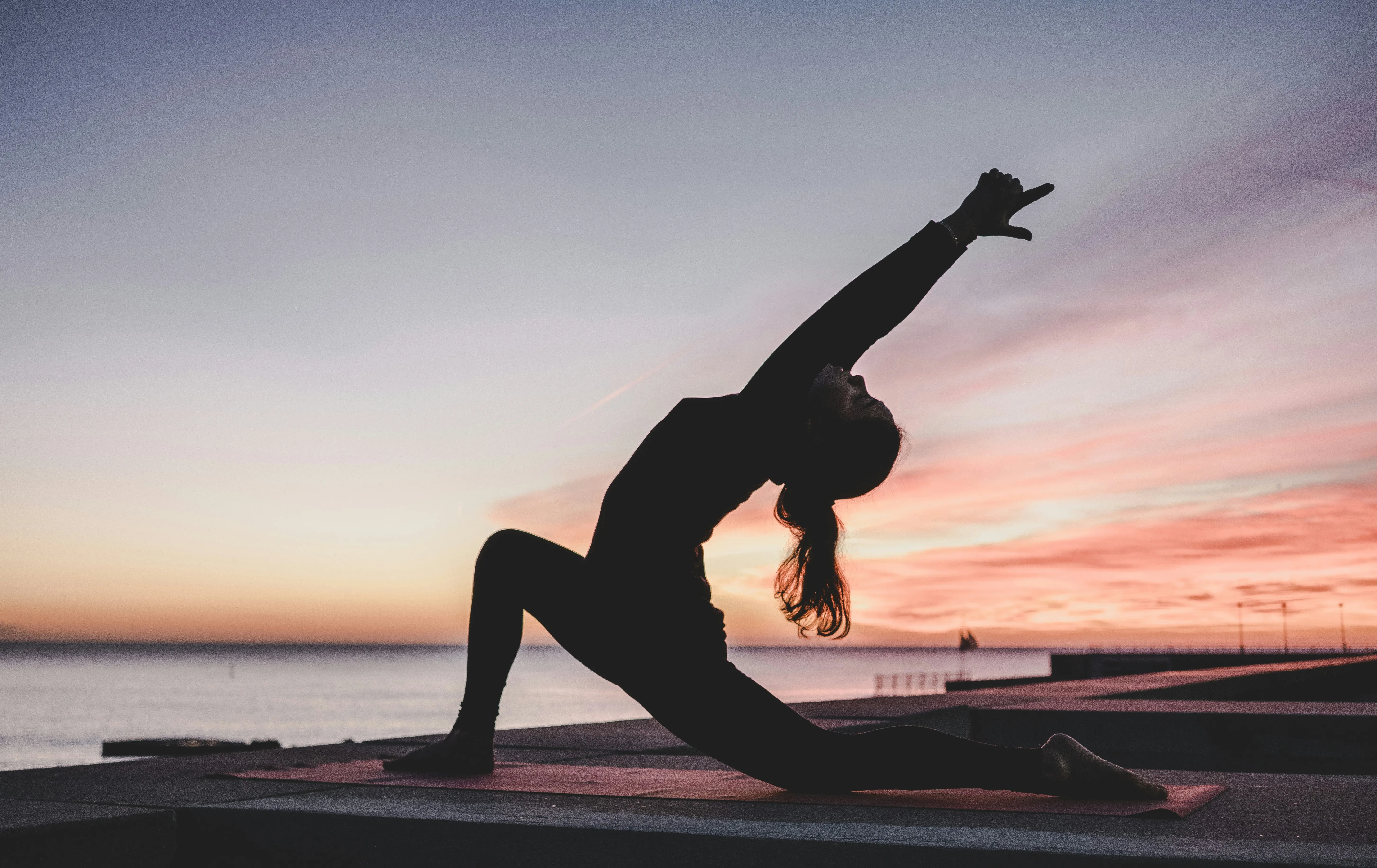 Overhead view of a woman mid-pose on a yoga mat across warm teak decking, long morning shadow stretching beside her